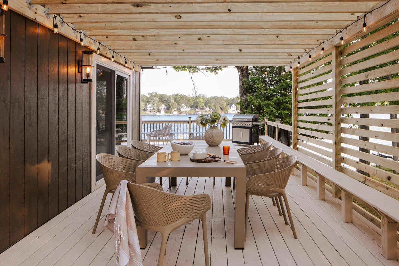 Photograph of the covered deck with string lights and a long table over the lake, built